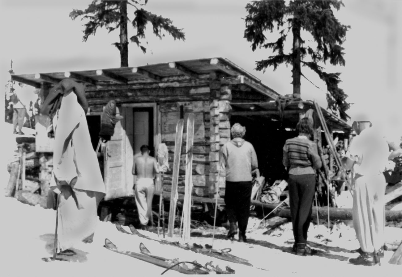 Historische Schwarz-Weiß-Aufnahme der ersten Breiteckalm-Hütte von 1952 mit Skifahrern und Holzski davor.
