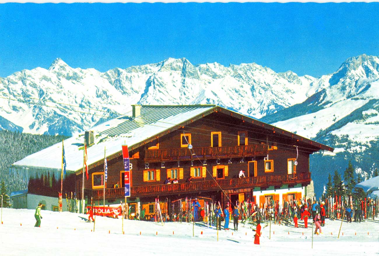Die Breiteckalm im Jahr 1976 mit Wintergästen vor dem Haus und Blick auf die Bergkette.